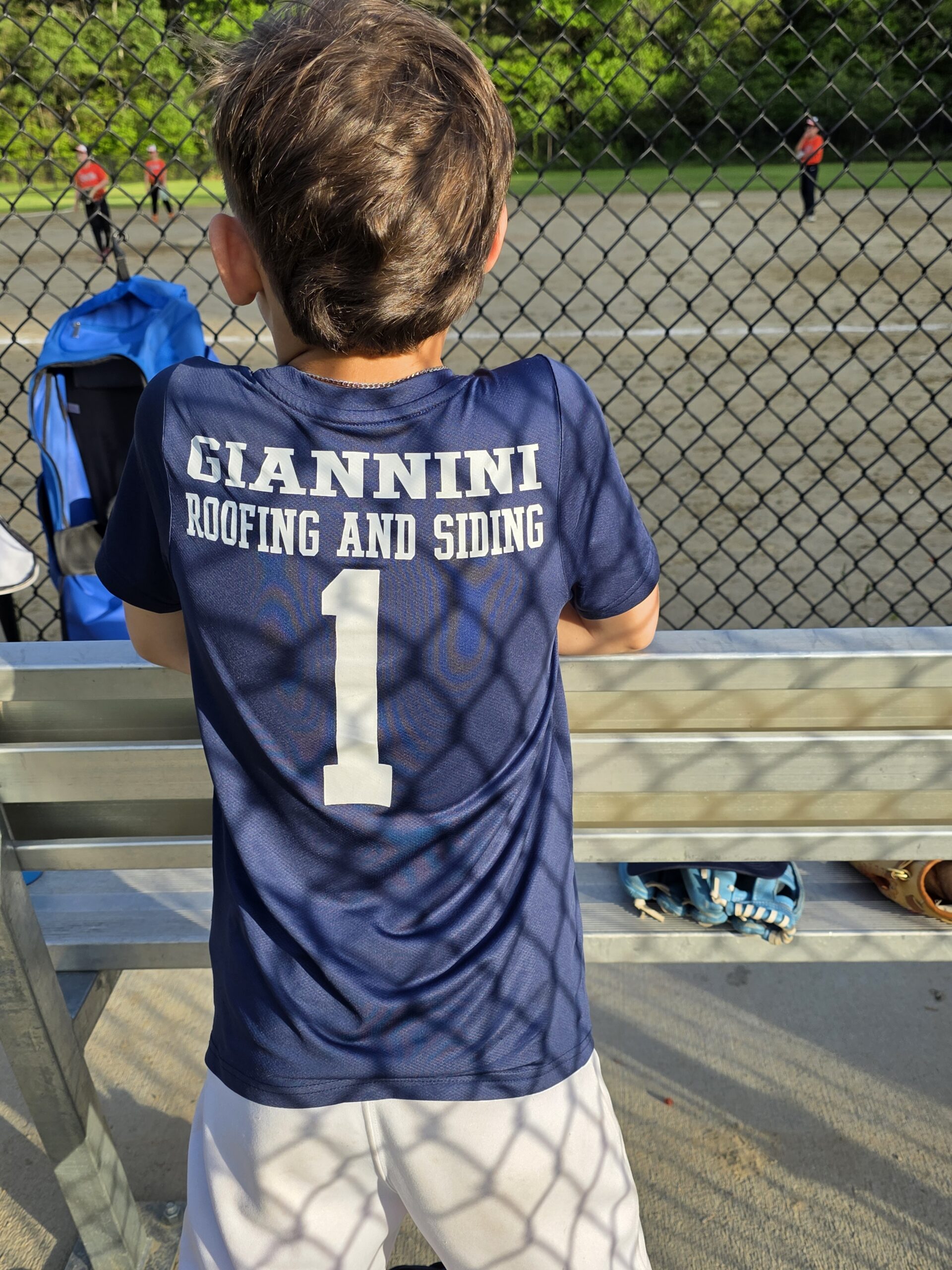 Close-up of an Abington Little League player wearing the navy Giannini Roofing and Siding number 1 jersey in the dugout